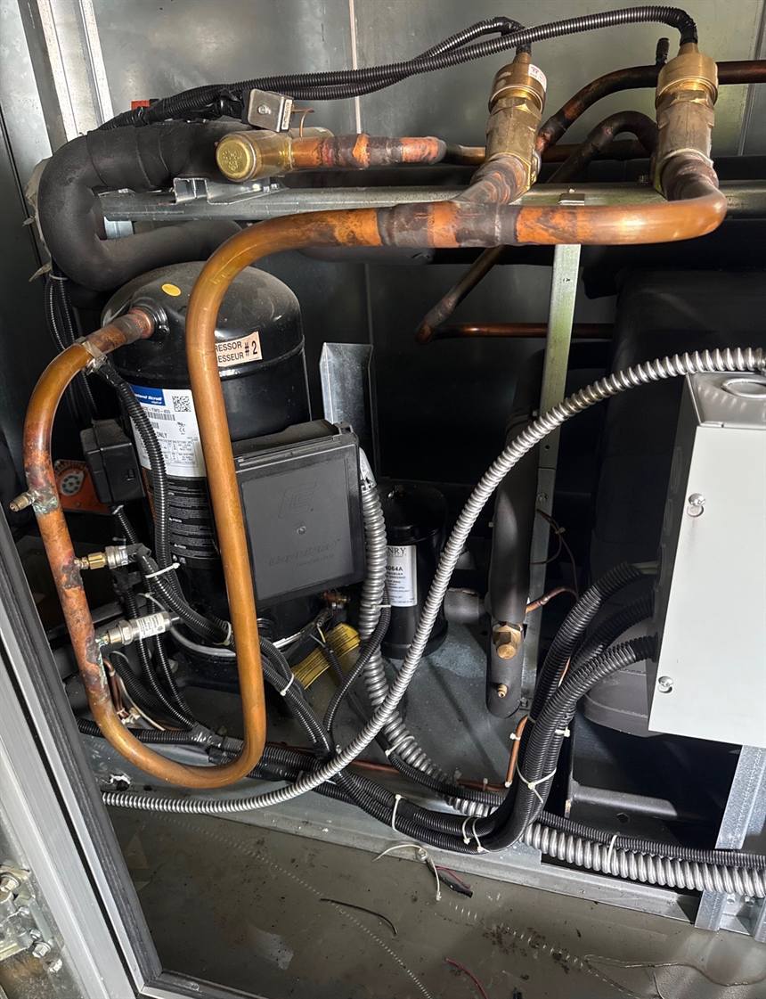 Brazed copper refrigerant piping routed around a scroll compressor inside a condensing unit.