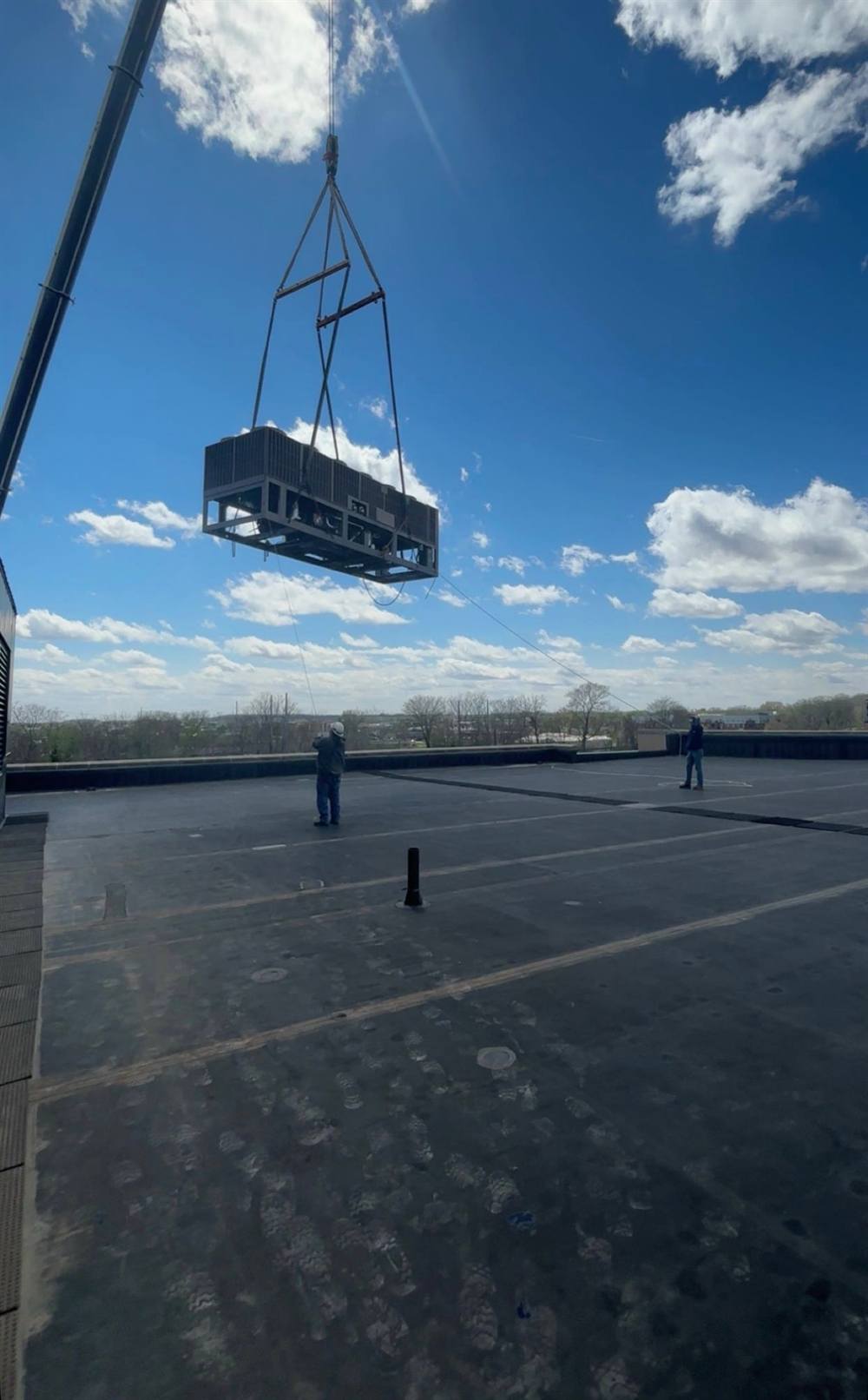 An RSI Mechanical crew guiding a rooftop unit into position on tag lines as a crane lowers it onto a commercial building.
